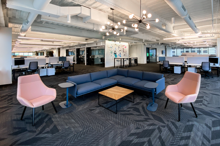 我们西雅图办公地点的广角镜头，包括沙发，椅子和开放式办公桌区域。