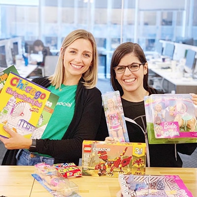 两名女性斯普劳特员工拿着慈善周收集的玩具摆姿势爱游戏体育官网首页